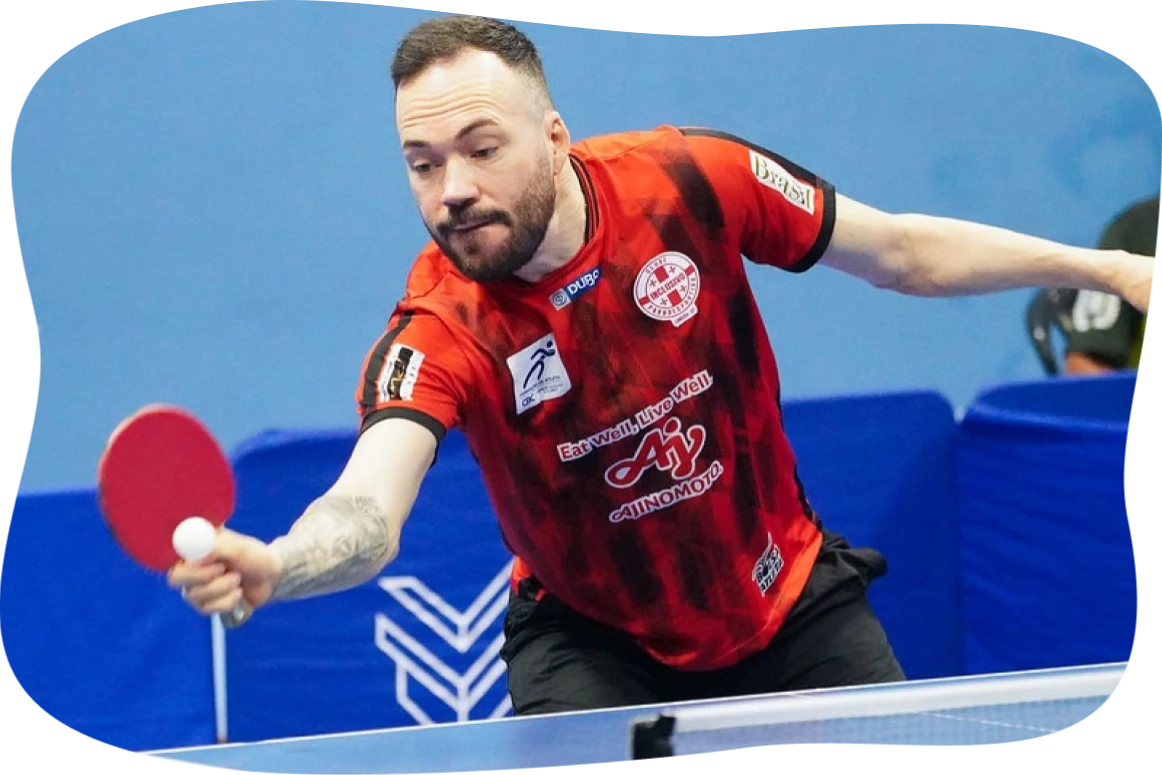 Esportista com uniforme vermelho jogando ping-pong em quadra