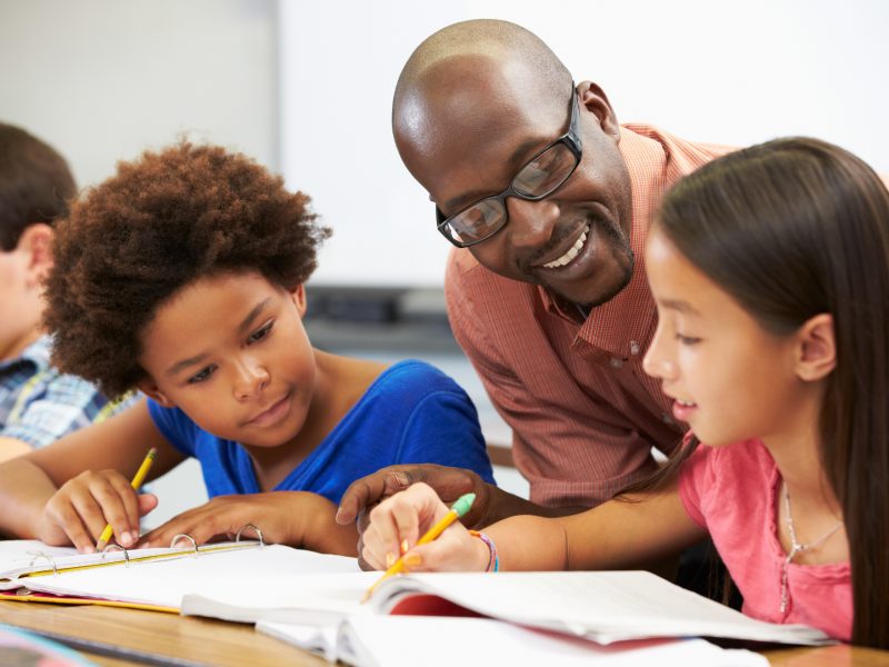 Close de um professor adulto e duas alunas crianças estudando e sorrindo